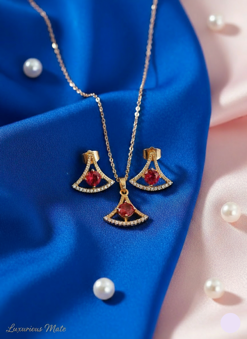Gold jewelry set with red gemstones on a blue fabric background