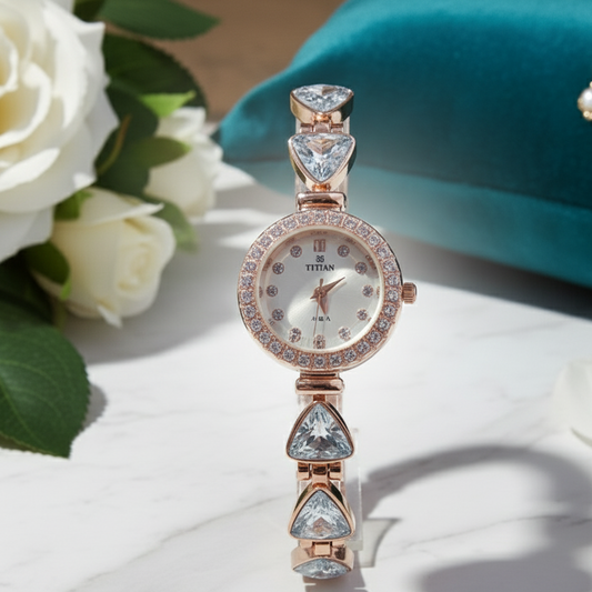 Rose gold watch with gemstones on a white surface with flowers and a teal object in the background