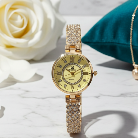 Gold wristwatch with diamond accents on a marble surface with a white rose and teal pillow in the background.
